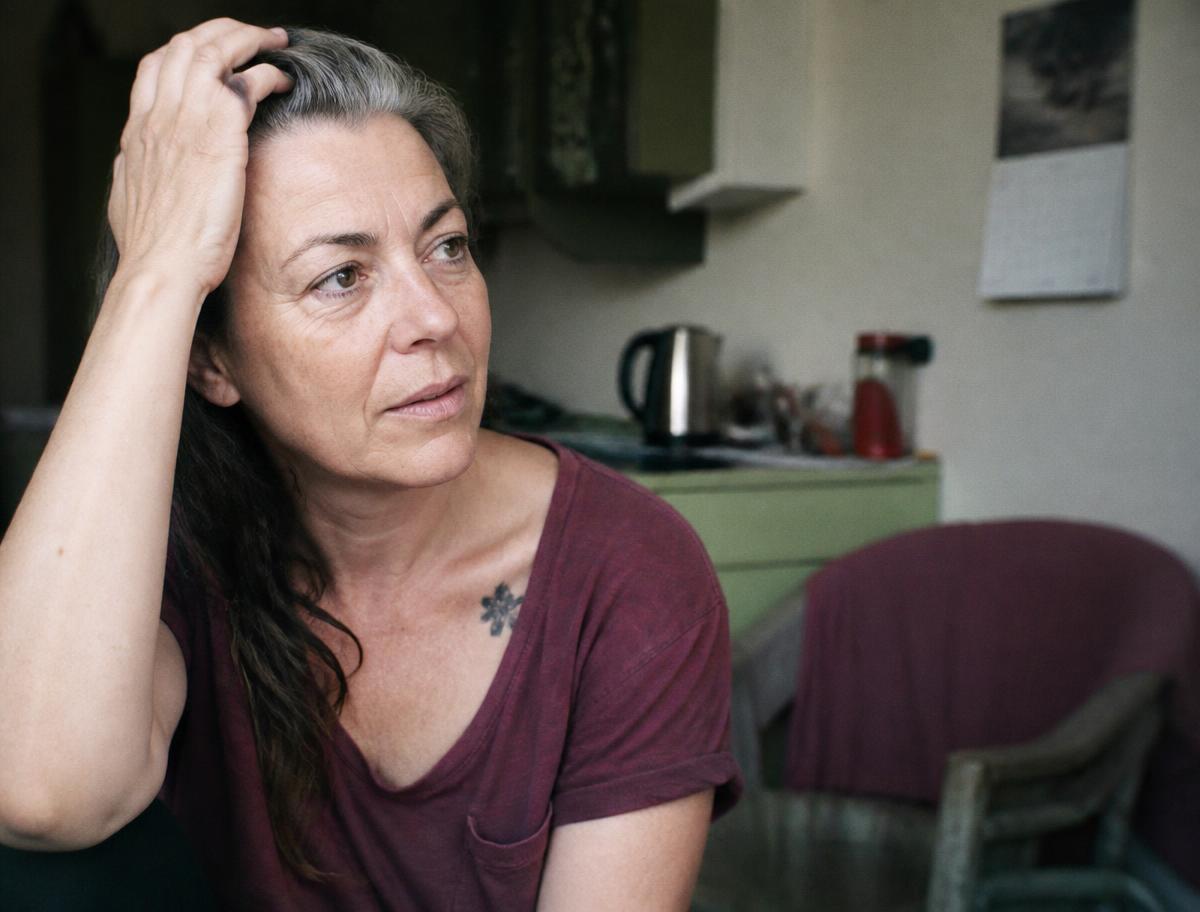 A midlife woman in a kitchen, calm, holding a mug, mid-thought.